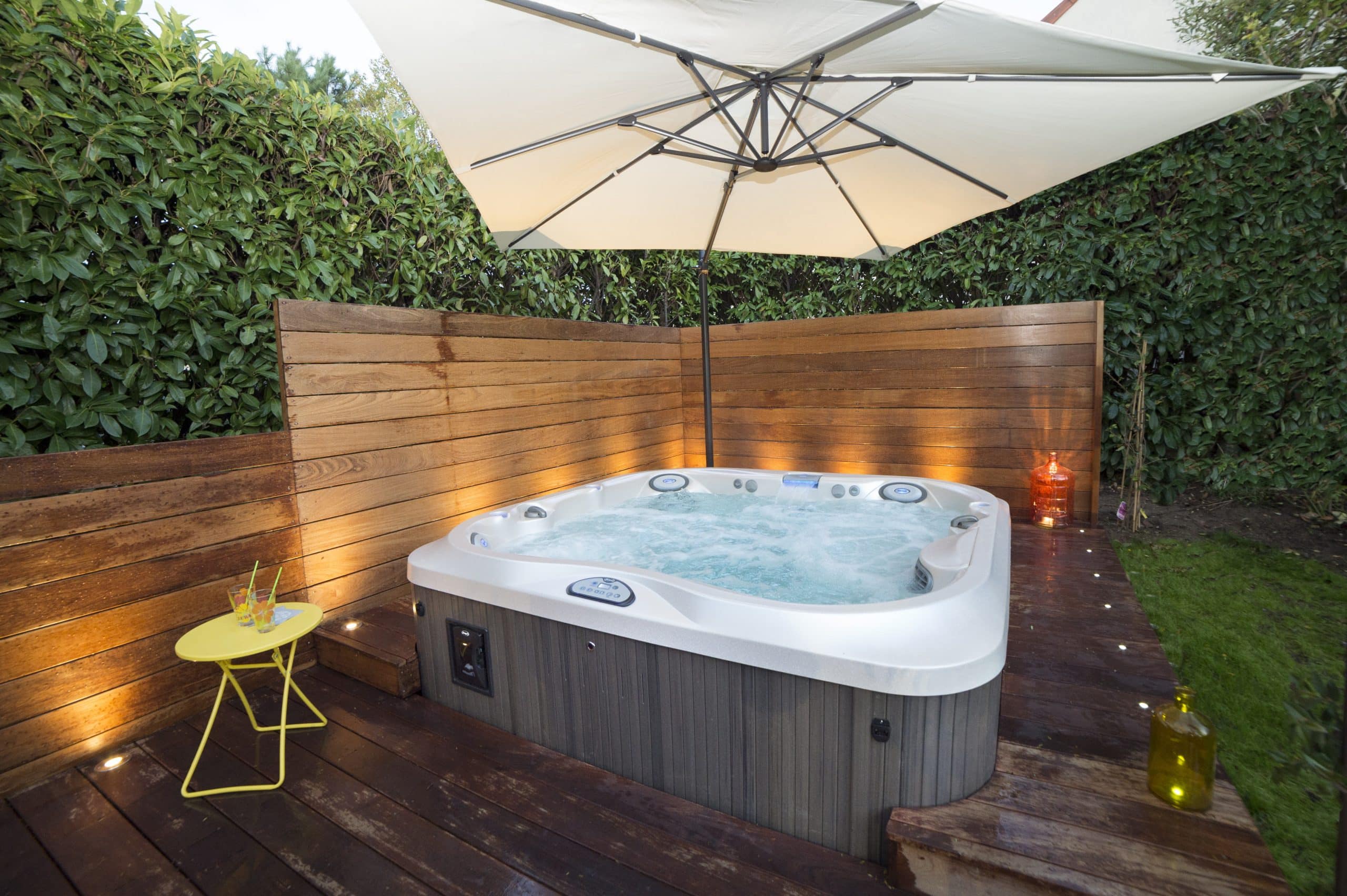 Jacuzzi hot tub in a backyard patio with chairs and umbrella