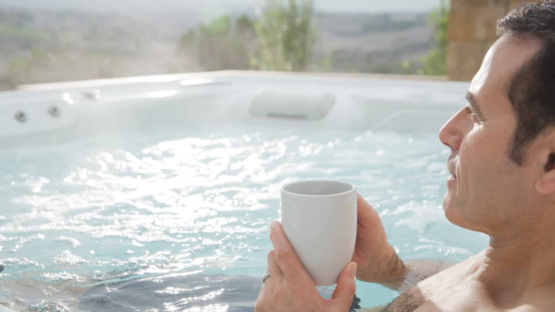a man sitting in a HotSpring hot tub holding a mug of coffee, reaping the top 3 benefits of salt water hot tubs