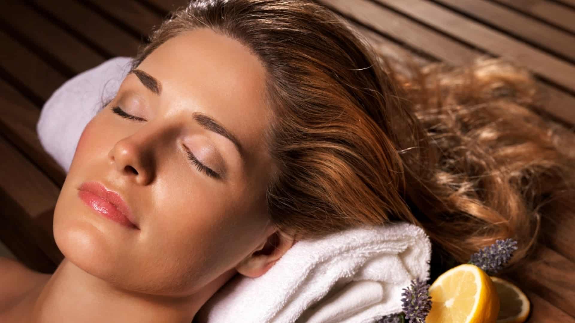 Improve your mental health with a sauna, like this woman laying down with her eyes closed and head on a towel.