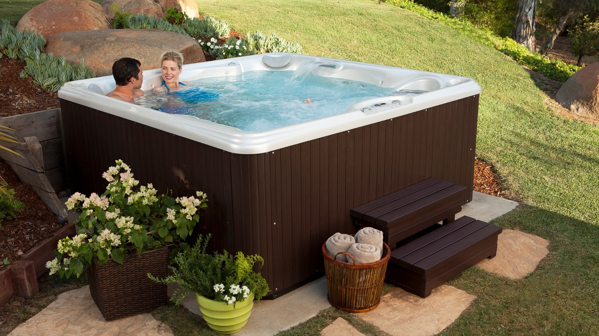 After thinking about 3 things to consider before situating your hot tub, this couple decided to place their hot tub outside within some rocky landscaping.